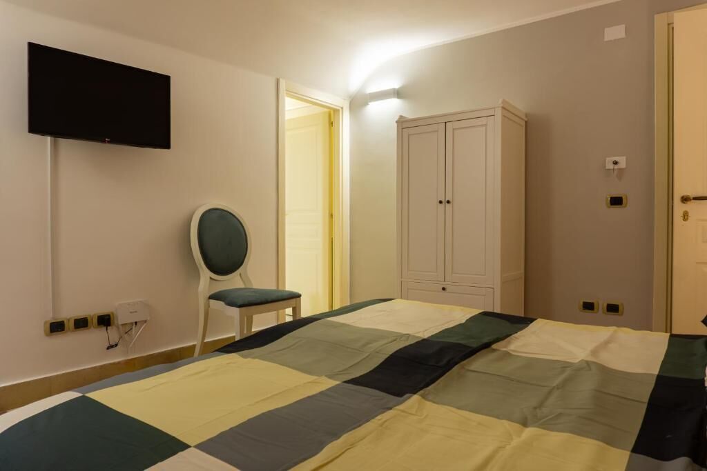 A bedroom with a bed, a chair, a wardrobe, and a television on the wall.