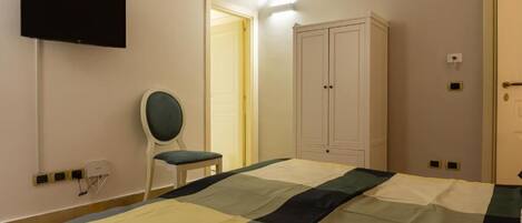A bedroom with a bed, a chair, a wardrobe, and a television on the wall.