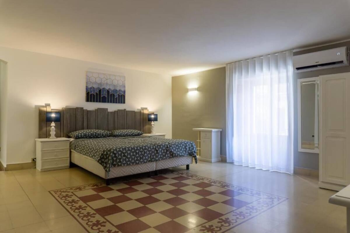 Un dormitorio con cama, mesitas de noche, una obra de arte en la pared, una lámpara de pie y una ventana con cortinas.