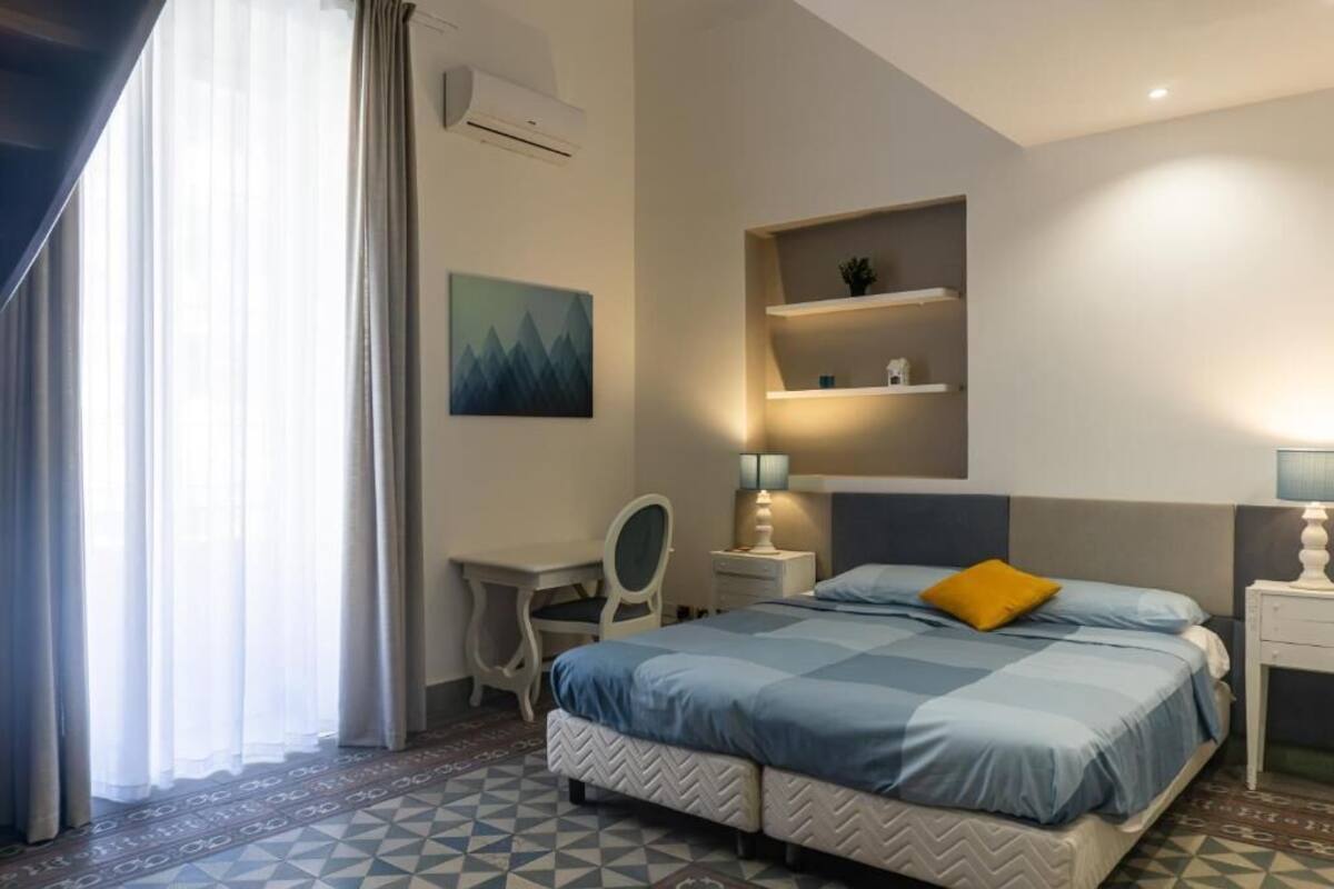 Una habitación de hotel con cama, escritorio, silla, estanterías y un cuadro.