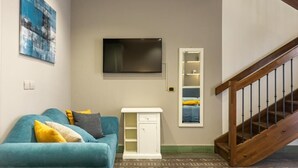 A living room with a teal sofa, a white cabinet, a mounted TV, and a wooden staircase. - Mi Tú Apartments (Catania)