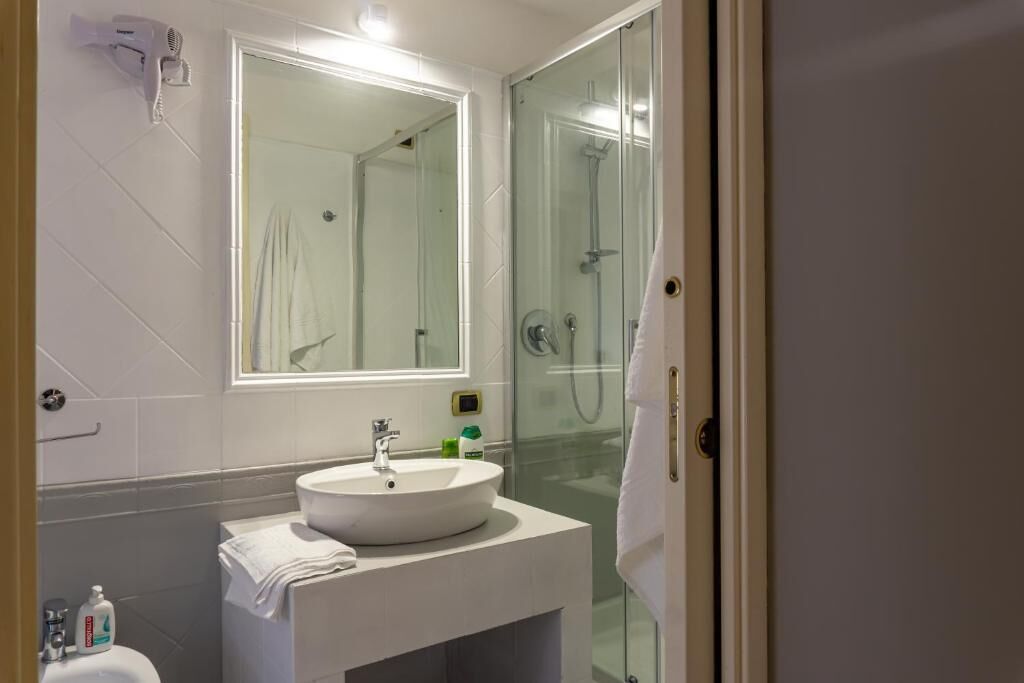 Un baño con cabina de ducha de vidrio, un lavabo blanco y un espejo encima.