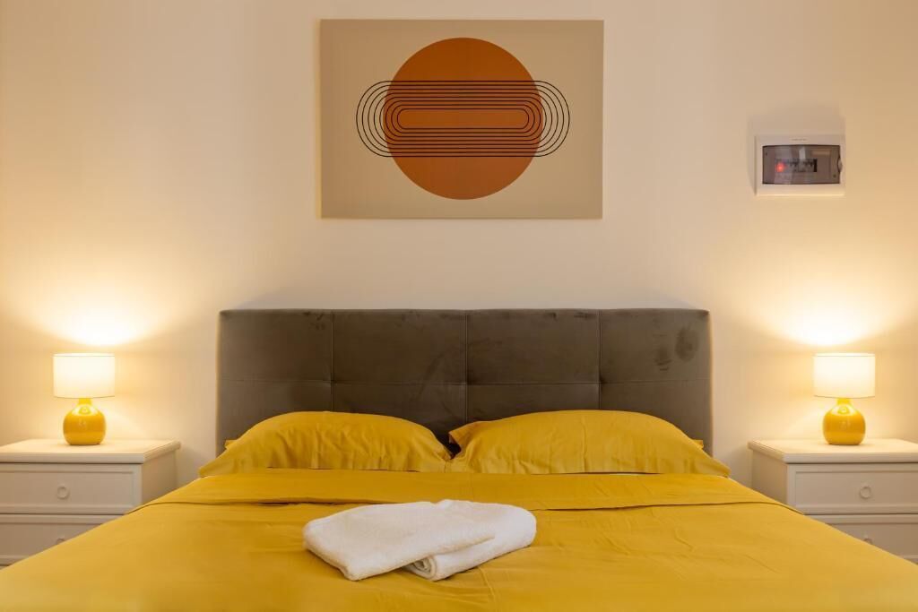 A hotel room with a bed, two bedside lamps, a thermostat, and a wall art piece.
