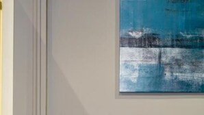 A teal sofa with two pillows, a wall-mounted light switch, and a blue abstract painting. - Mi Tú Apartments (Catania)