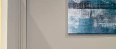 Un canapé de couleur turquoise avec deux coussins, un interrupteur fixé au mur et un tableau abstrait bleu.