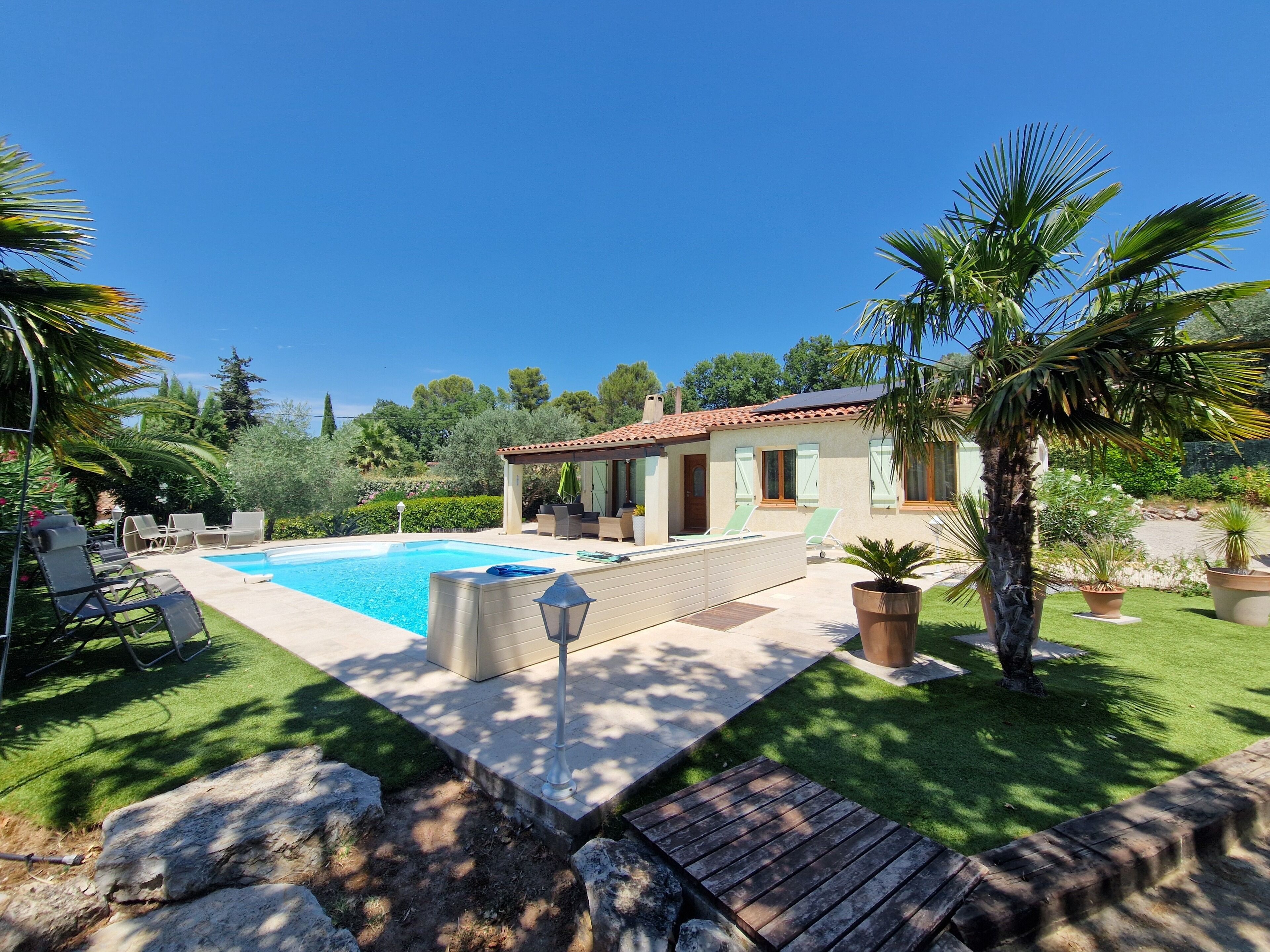 Une maison avec une piscine, un espace salon extérieur et un jardin.