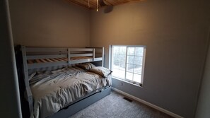 Un dormitorio con una cama individual superpuesta, una ventana y piso alfombrado.