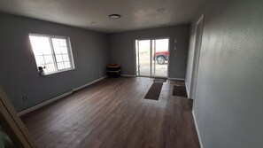 Ein geräumiges Zimmer mit Holzdielen, großen Fenstern und einer Schiebeglastür, die nach draußen führt.