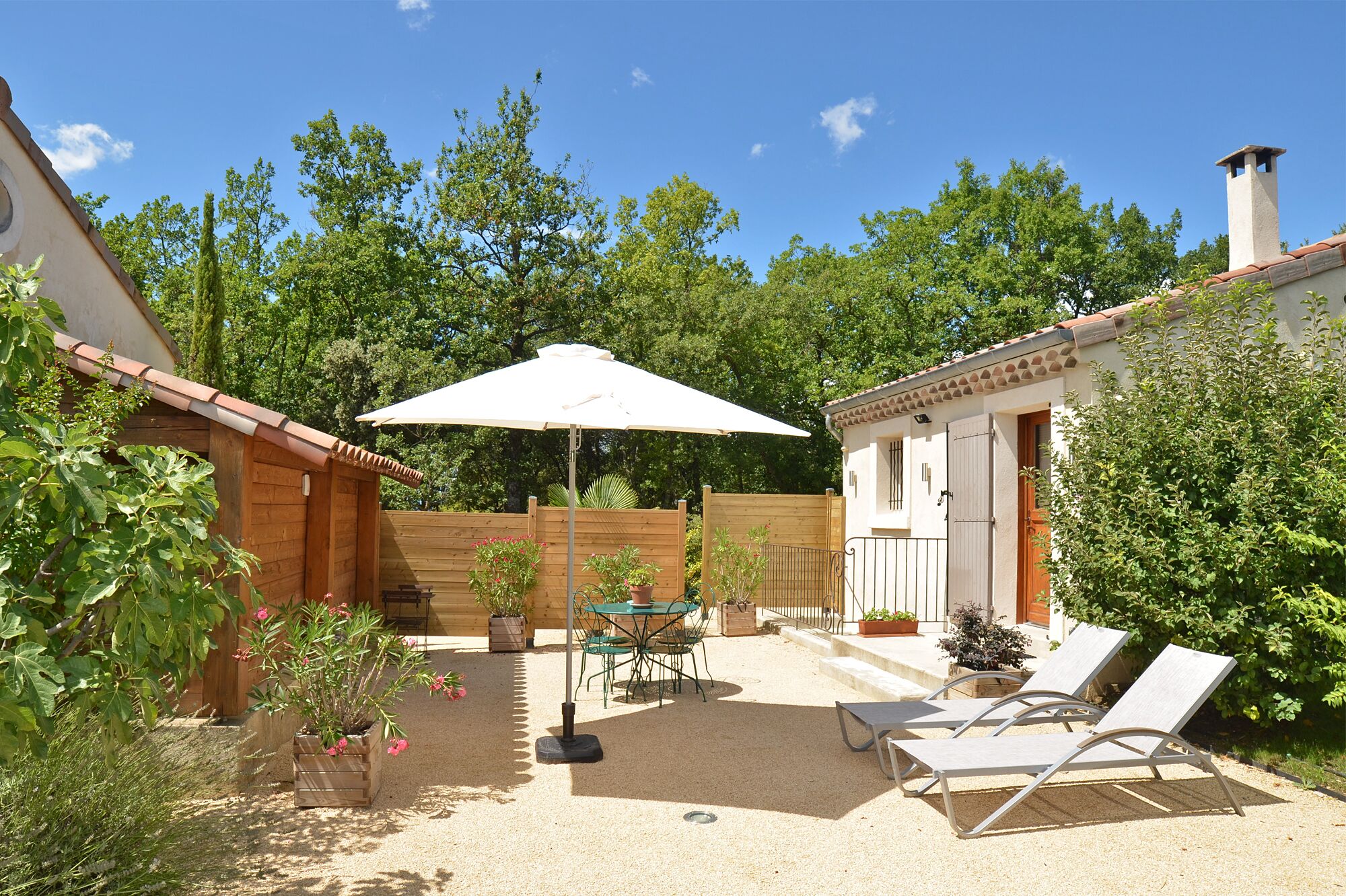 Een terras met een tafel en stoelen, een witte parasol, en een zithoek met lounge fauteuils.