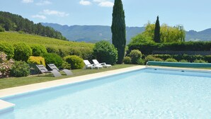 A swimming pool with lounge chairs, surrounded by lush greenery and mountains in the background. - Figuier Vacation Rental: Les Cerisiers 2, surrounded by nature near the Drôme River (Mirabel-et-Blacons)