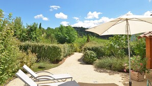 A garden path leading to a seating area with a large umbrella, surrounded by lush greenery and a clear sky. - Figuier Vacation Rental: Les Cerisiers 2, surrounded by nature near the Drôme River (Mirabel-et-Blacons)