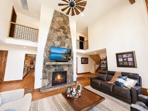 A spacious living area with a stone fireplace, a mounted TV, a leather sofa, and a wooden staircase. - Luxury Lake Tahoe Retreat, Designer Home, Chef's Kitchen, Lake View (SL171) (Stateline)