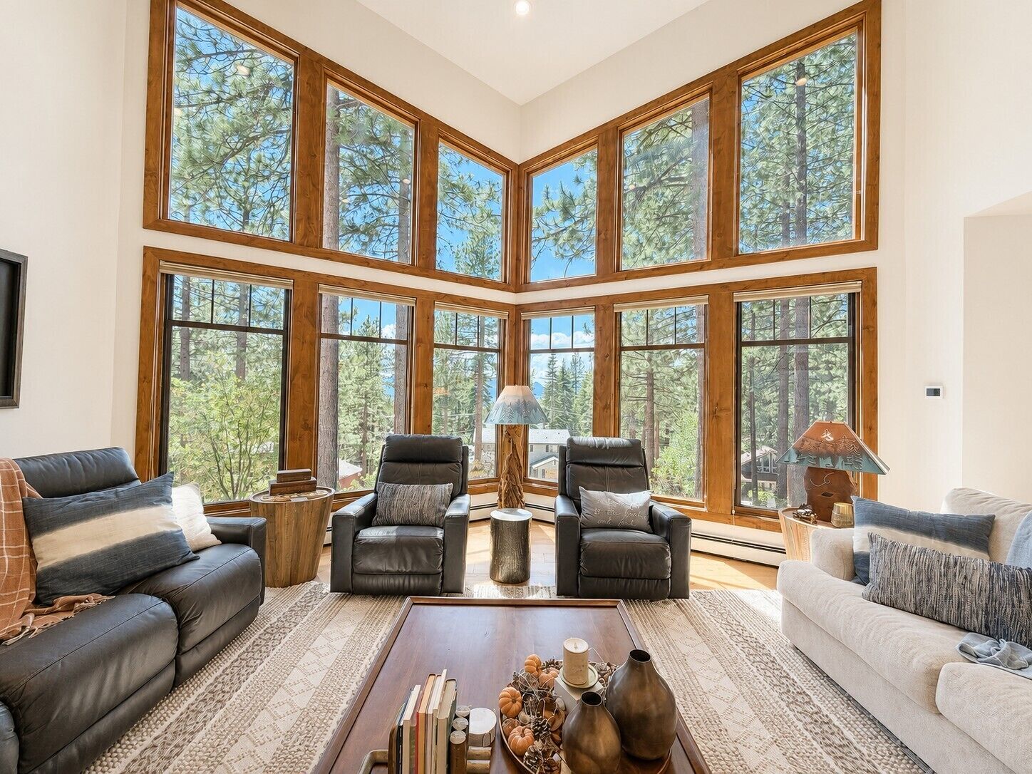 A spacious living room with large windows, leather sofas, a coffee table with decorative items, and a fireplace.