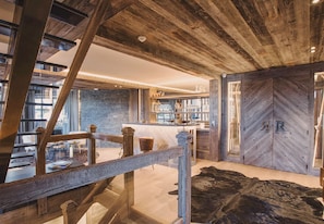 A rustic interior with exposed wooden beams, a stone wall, a bar area, and a large leather rug. - 5-Bedroom Chalet with Wellness Area (La Clusaz)