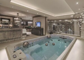 Una piscina interior luxosa amb zona de bar, televisió i una finestra gran amb vistes.