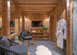 Ein Holzblockhaus-Interieur mit Fernseher, einem Sessel, einem kleinen Tisch, einer Topfpflanze und einem Handtuchhalter.