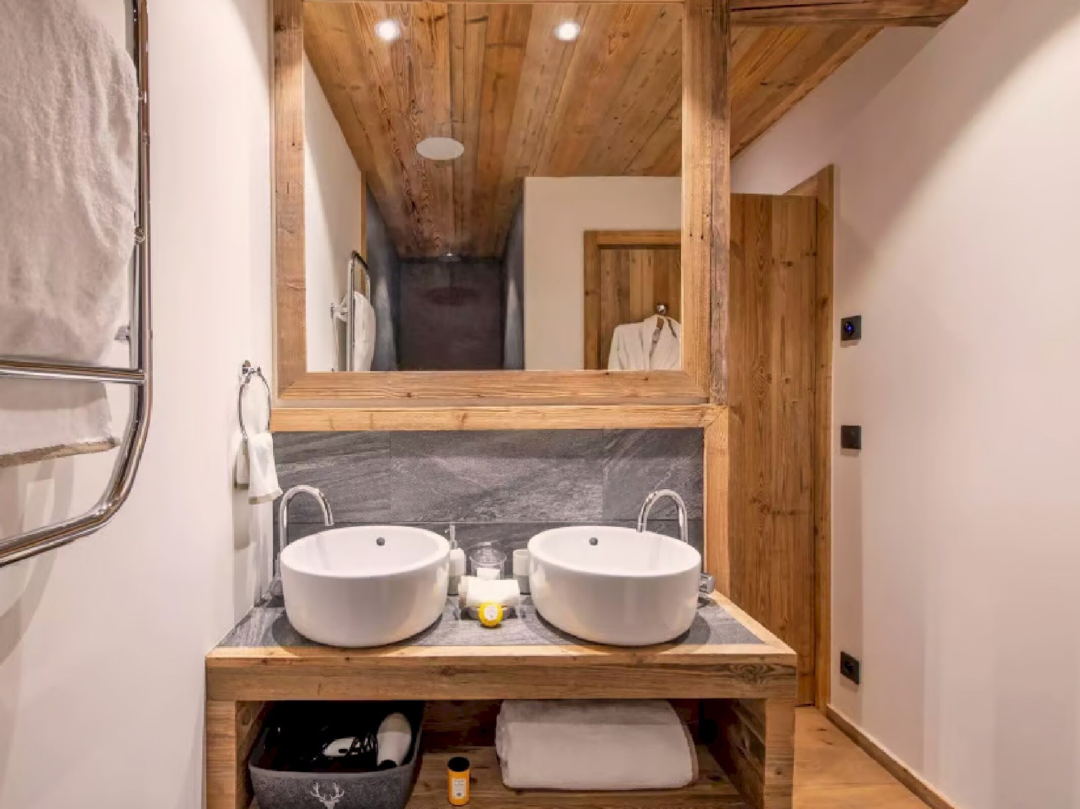 Un baño con dos lavamanos, un tocador de madera, un espejo y un perchero para toallas.