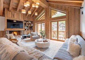 Ein gemütliches Wohnzimmer mit Kamin, Holzbalken, einem großen Fernseher und Blick ins Freie.