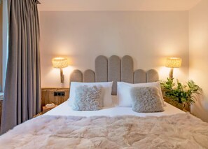 Ein Bett mit flauschig-weißer Bettwäsche, zwei Wandleuchten und ein Kopfteil mit einem außergewöhnlichen Design.