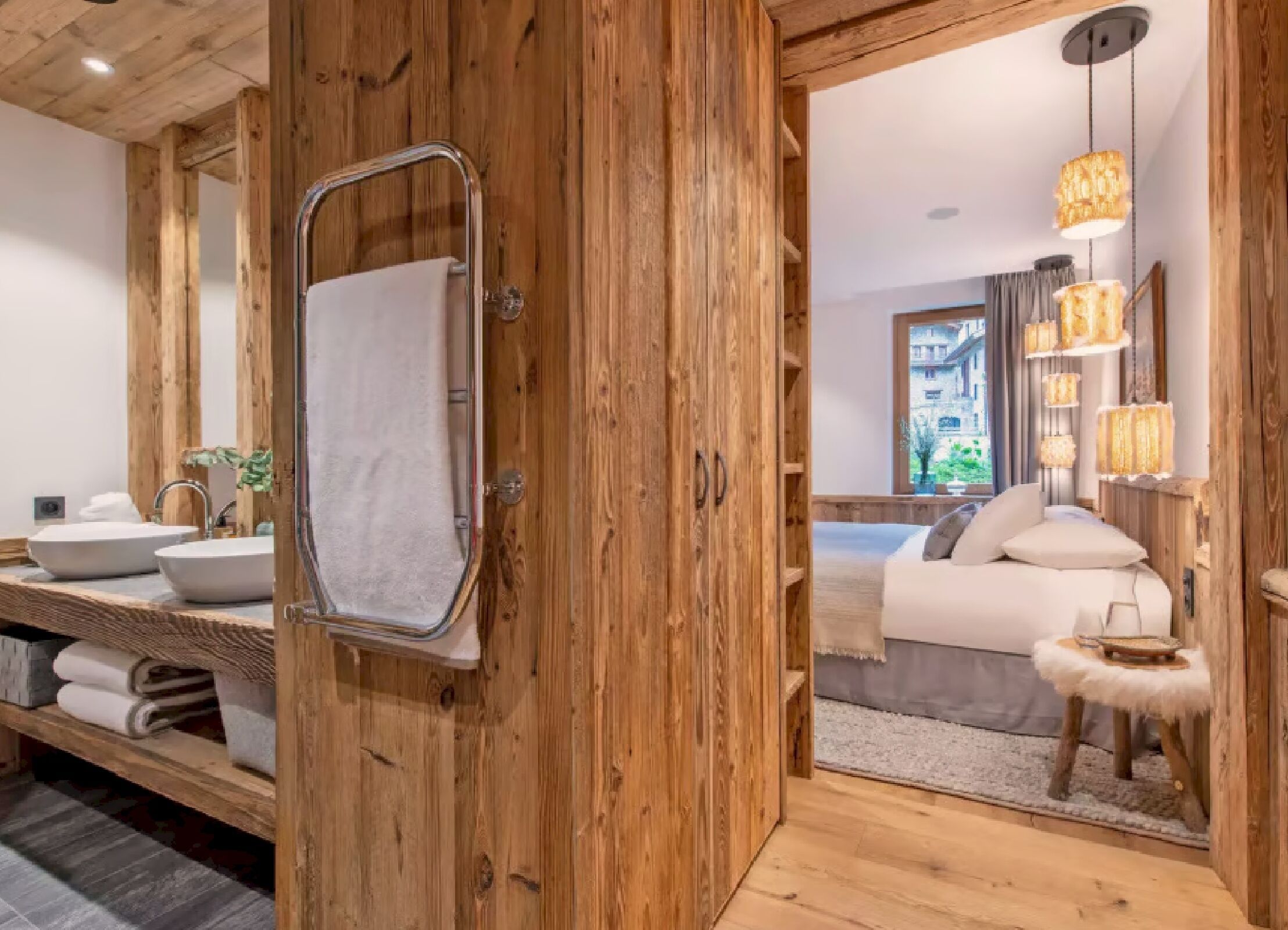 Une porte en bois donne accès à une salle de bain équipée d’un miroir, de deux lavabos et d’un porte-serviettes.