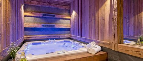 Interior de una cabaña de madera con un jacuzzi, escalones de madera y un espejo que refleja la habitación.