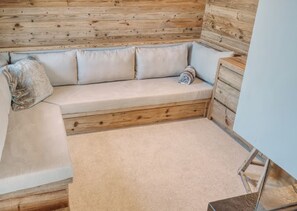 Eine Holzbänkchen mit Kissen, ein kleiner Holzschrank und ein Teppichboden.