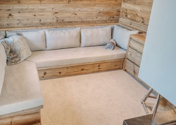 A wooden bench with cushions, a small wooden cabinet, and a carpeted floor.
