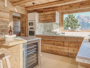 Eine Holzhütte mit einer Küchenzeile, einem großen Fenster, eingebauten Backöfen und einem Weinkühler.