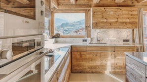 A kitchen with wooden cabinets, a Bosch oven, a marble countertop, and a view of a town through a window. - 5-Bedrooms Chalet with Views (Les Allues)
