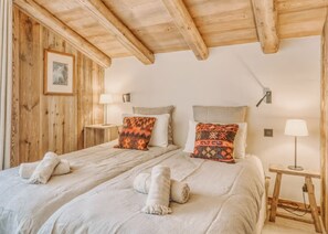 A room with two beds, wooden walls, a framed picture, two bedside tables with lamps, and a wooden ceiling.
