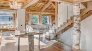 A modern interior with wooden beams, a glass staircase, and a seating area with white furniture. - 5-Bedrooms Chalet with Views (Les Allues)