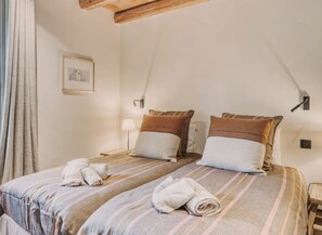 A double bed with striped bedding and two pillows, a bedside table with a lamp, a framed picture on the wall, and a window with curtains.
