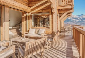 Eine Holzterrasse mit Gartenmöbeln, einer Treppe und Blick auf die Berge.