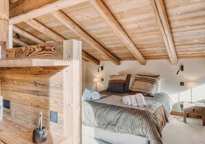 Eine Holzbalkendecke, ein Bett mit gestreifter Bettwäsche und ein Nachttisch mit einer Lampe.