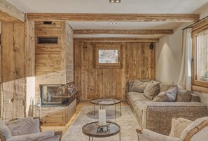 Une pièce chaleureuse avec des murs en bois, une cheminée, un canapé et deux petites tables d’appoint.