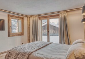 Een slaapkamer met een bed, gordijnen, een raam en uitzicht op een besneeerd landschap.