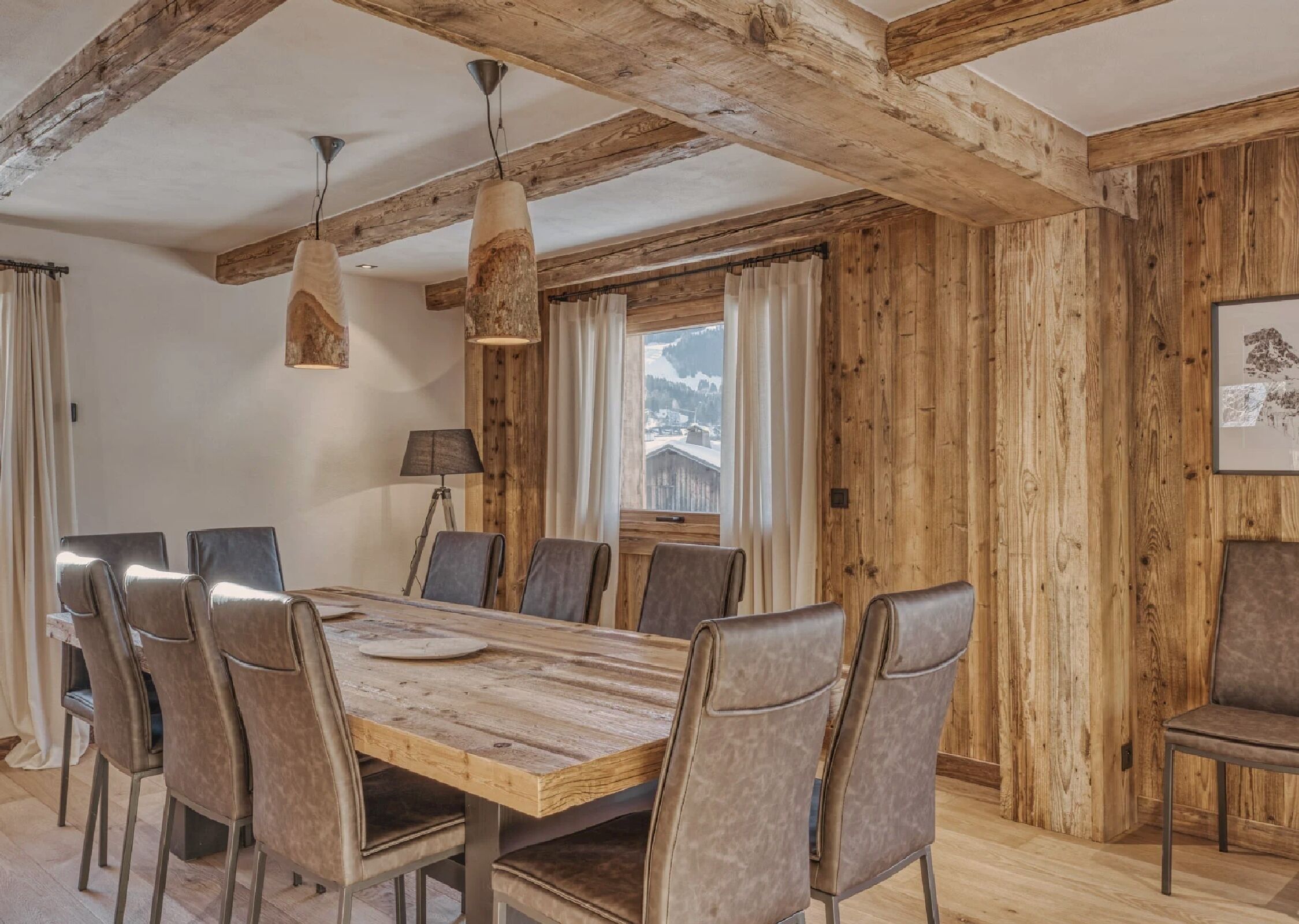 Ein Essbereich mit Holztisch und -stühlen, Holzbalken an der Decke und einem Fenster mit Bergblick.