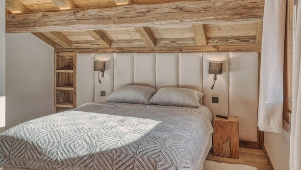 Ein Schlafzimmer mit Holzboden, einem Bett mit gemustertem Überwurf, zwei Wandlampen und einem Nachttisch aus Holz.