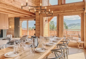 A wooden dining area with a table set for six, large windows, and a view of the outdoors.