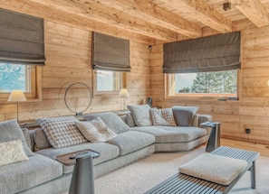 A cozy log cabin interior with a sectional sofa, two lamps, a round mirror, and a view of the outdoors.