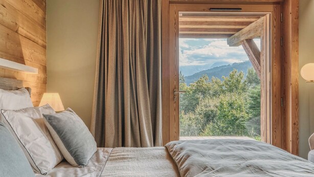 A bedroom with a bed, pillows, a window with curtains, and a view of mountains. - Modern Chalet with Panoramic Views (Les Avanchers-Valmorel)
