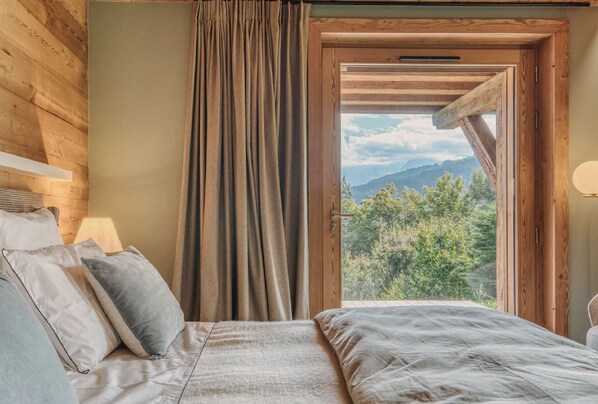 A bedroom with a bed, pillows, a window with curtains, and a view of mountains.