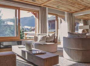Ein modernes Interieur mit großen Fenstern, einem Sofa, einem runden Hocker und einem Holztisch.