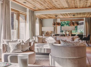 Ein geräumiges Wohnzimmer mit hohen Decken, großen Fenstern und Blick auf Grünflächen.
