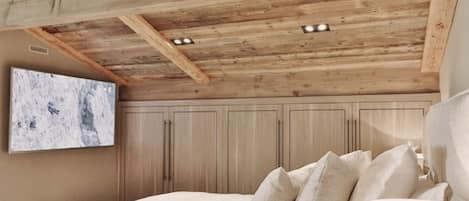 Un dormitorio con vigas de madera en el techo, una cama con almohadas, una lámpara de pared y un ventanal grande.