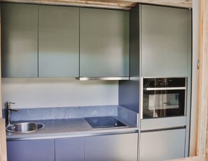 Eine kompakte Küche mit Backofen, Spülbecken aus Edelstahl und grauen Schränken.