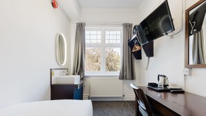 Een hotelkamer met een bed, een bureau, een televisie, een spiegel en een raam met gordijnen.