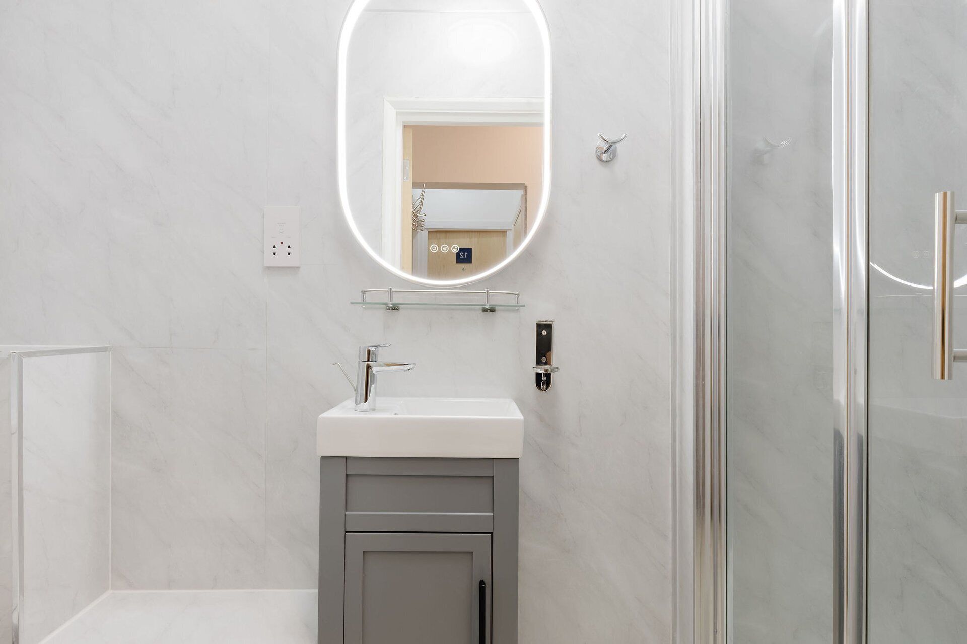 A modern bathroom with a glass shower enclosure, a white sink with a chrome faucet, and a mirror with a light.