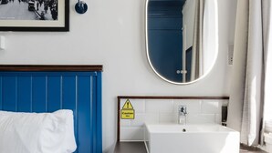 A hotel room with a bed, a white sink, a mirror, and a caution sign.
