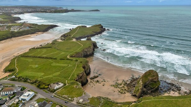 Un paysage côtier comprenant une plage, des zones herbeuses et une route menant à un ensemble de bâtiments.